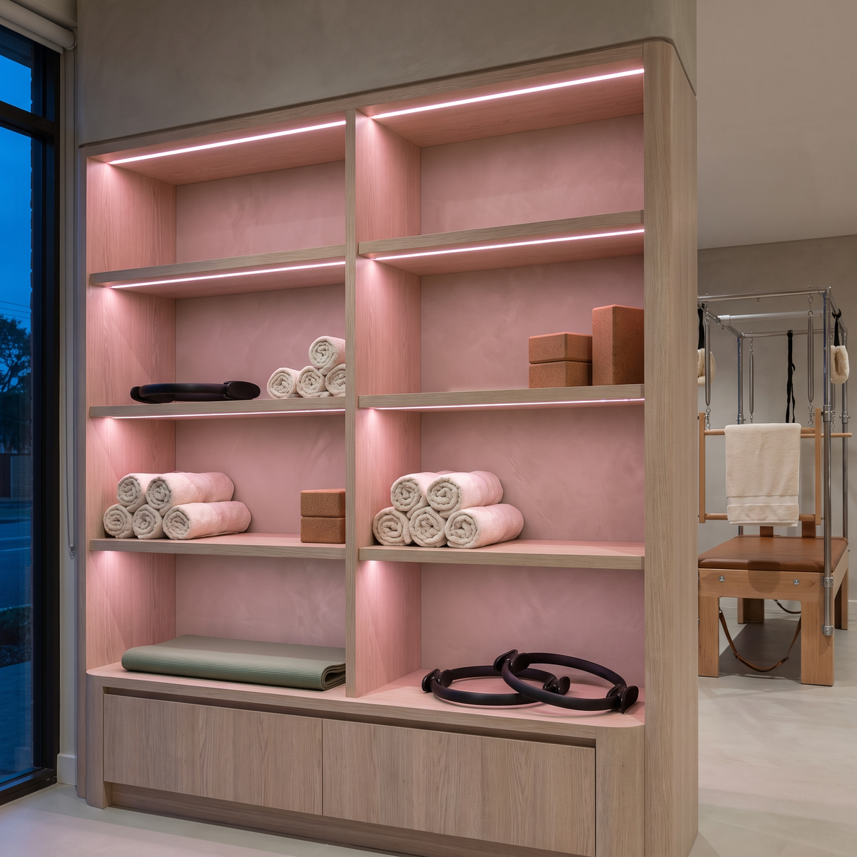 Pink dot-free LED strip lighting beneath bleached-oak equipment shelves in a Pilates studio