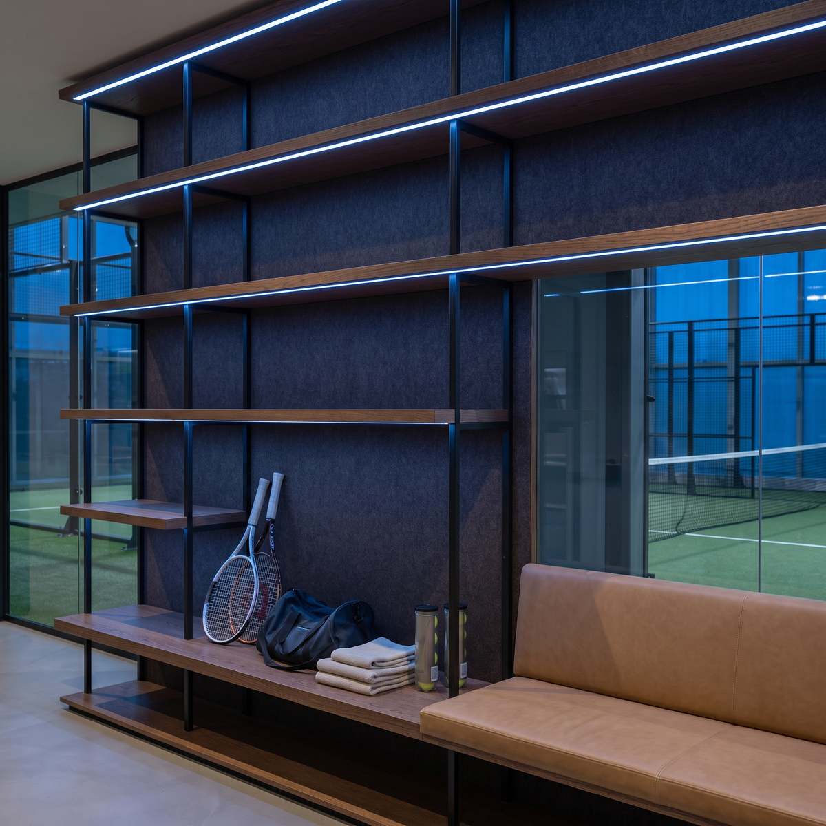 Blue dot-free LED strip lighting beneath dark-oak equipment shelves in a racquet sports club