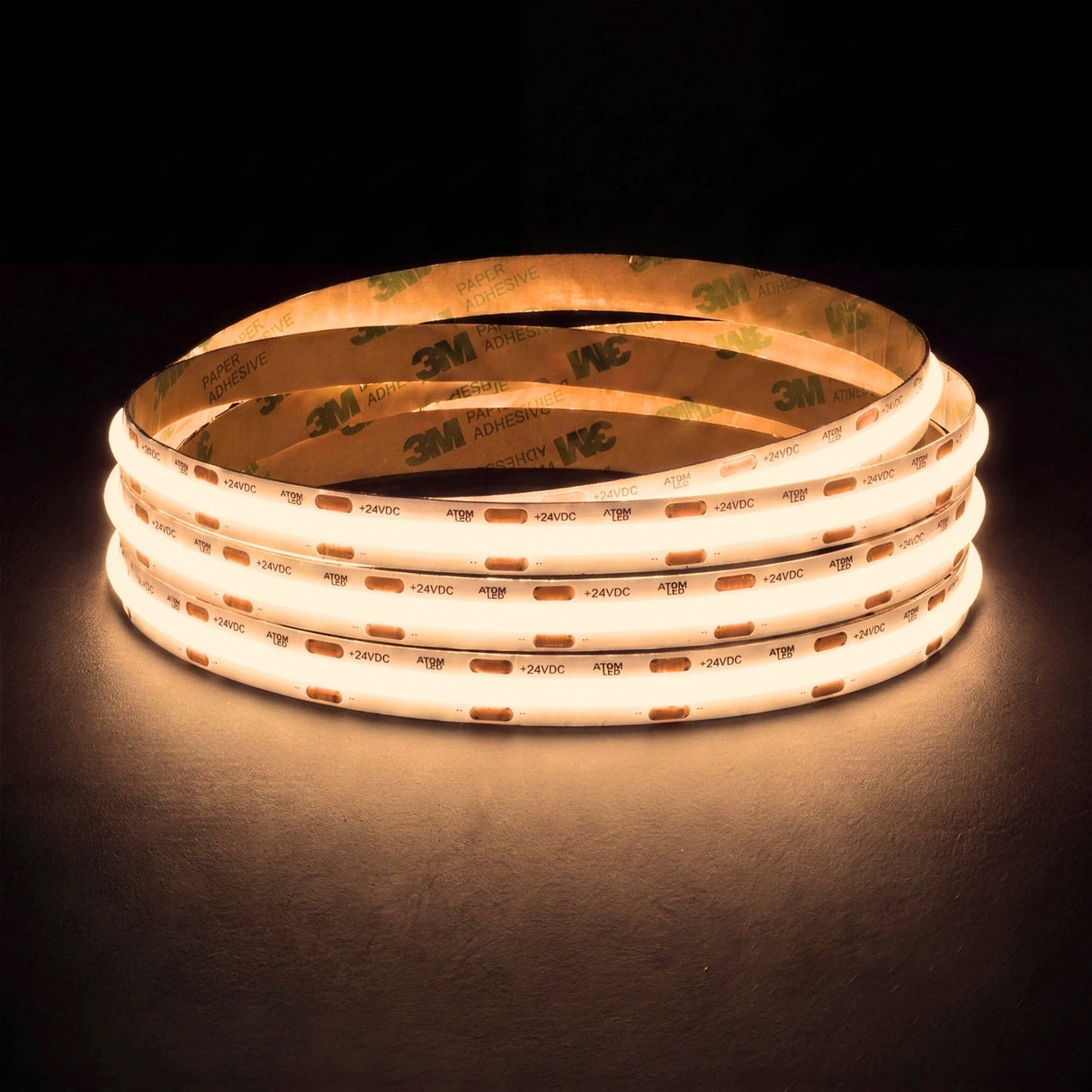 Warm white 3000K SCOB LED strip coil illuminated on a dark background, 24V DC and 10mm wide, with copper connection pads