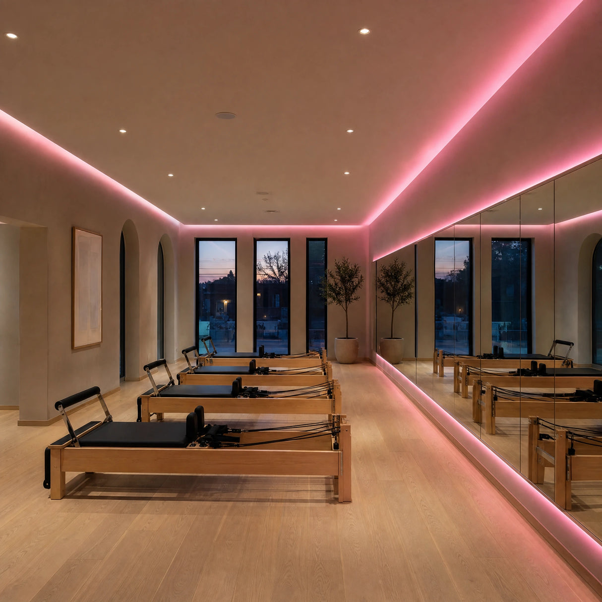 Illustrative Pilates studio with pink SCOB LED ceiling-cove lighting, a backlit mirror and timber reformer machines