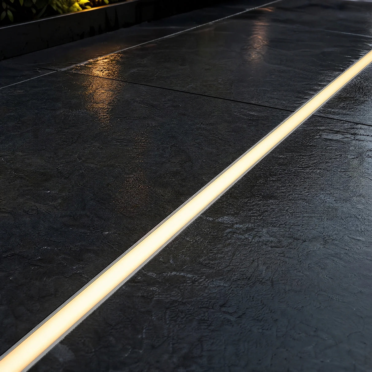 LED floor profile set flush into dark paving, lit warm white at dusk