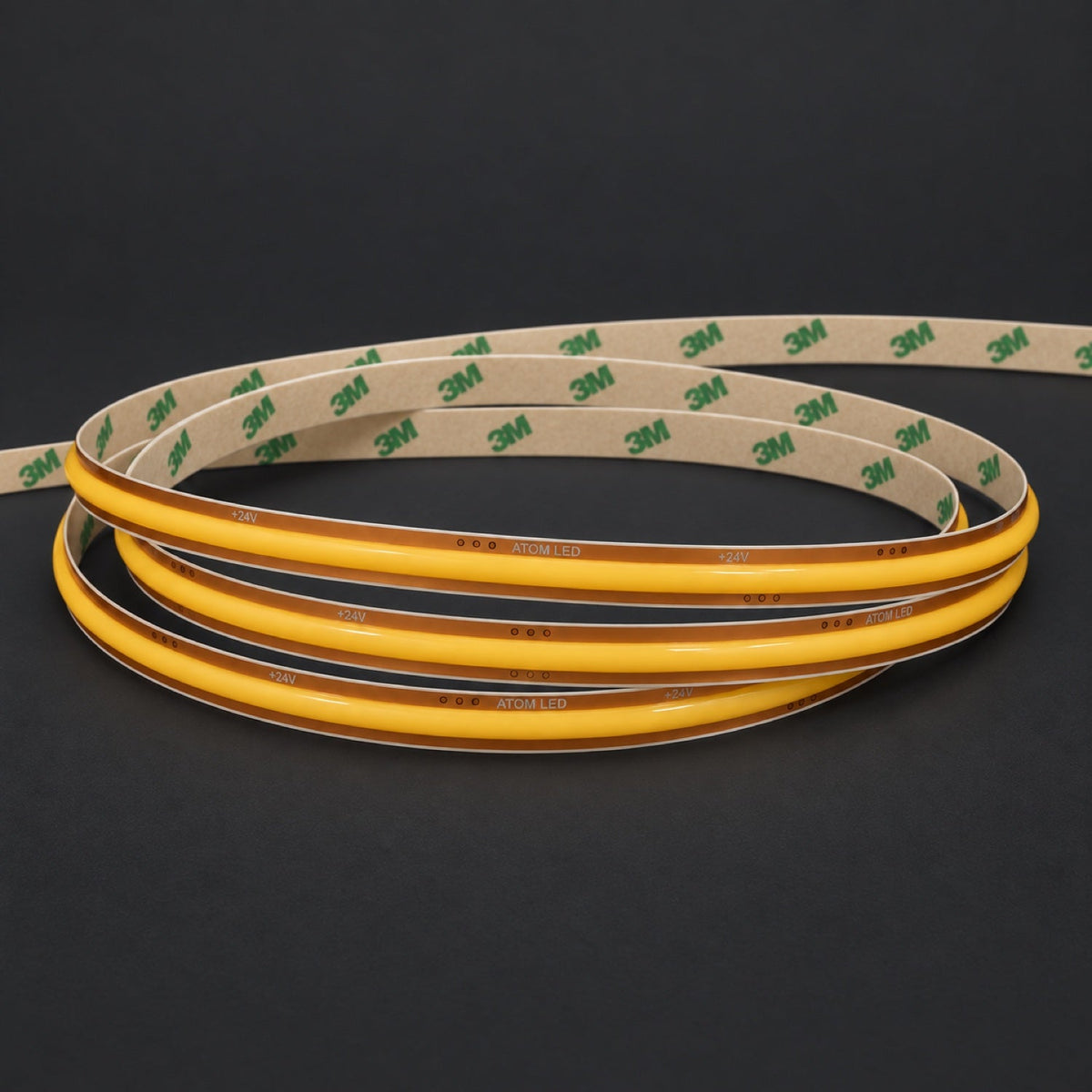 ATOM LED FreeCut COB LED strip switched-off coil with golden PCB and 3M Tape backing on charcoal background