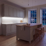 Daylight 5000K COB LED strip lighting beneath wall cabinets in a large British kitchen in the evening; installation illustration.