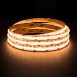 Warm white 2700K SCOB LED strip coil illuminated on a dark background, 24V DC and 10mm wide, with copper connection pads
