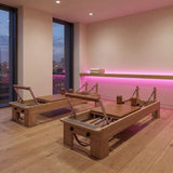 Pink SCOB LED strip accent lighting behind an oak ledge in a Pilates studio with two reformers; installation illustration.